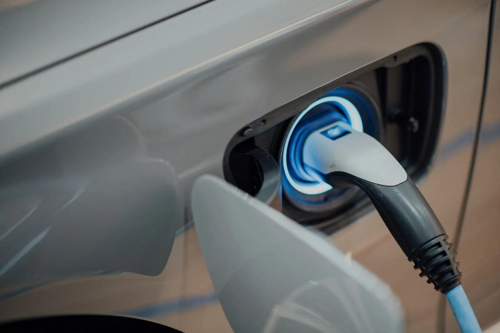 Ladestecker steckt im blau beleuchteten Ladeanschluss eines silbernen Elektroautos