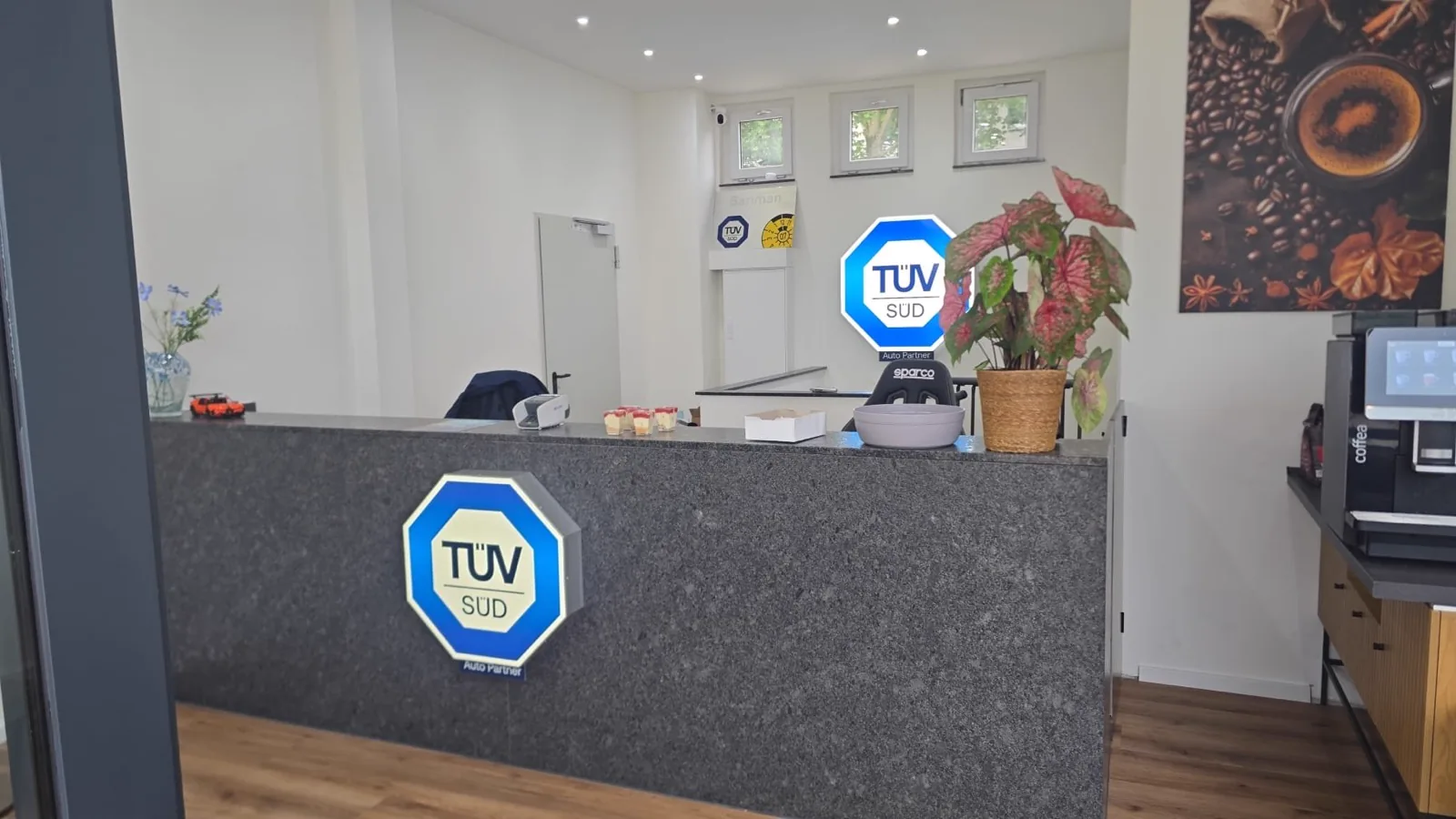 Empfangstresen aus Granit mit TÜV-SÜD-Zeichen, dahinter der Arbeitsplatz, rechts die Kaffeemaschine