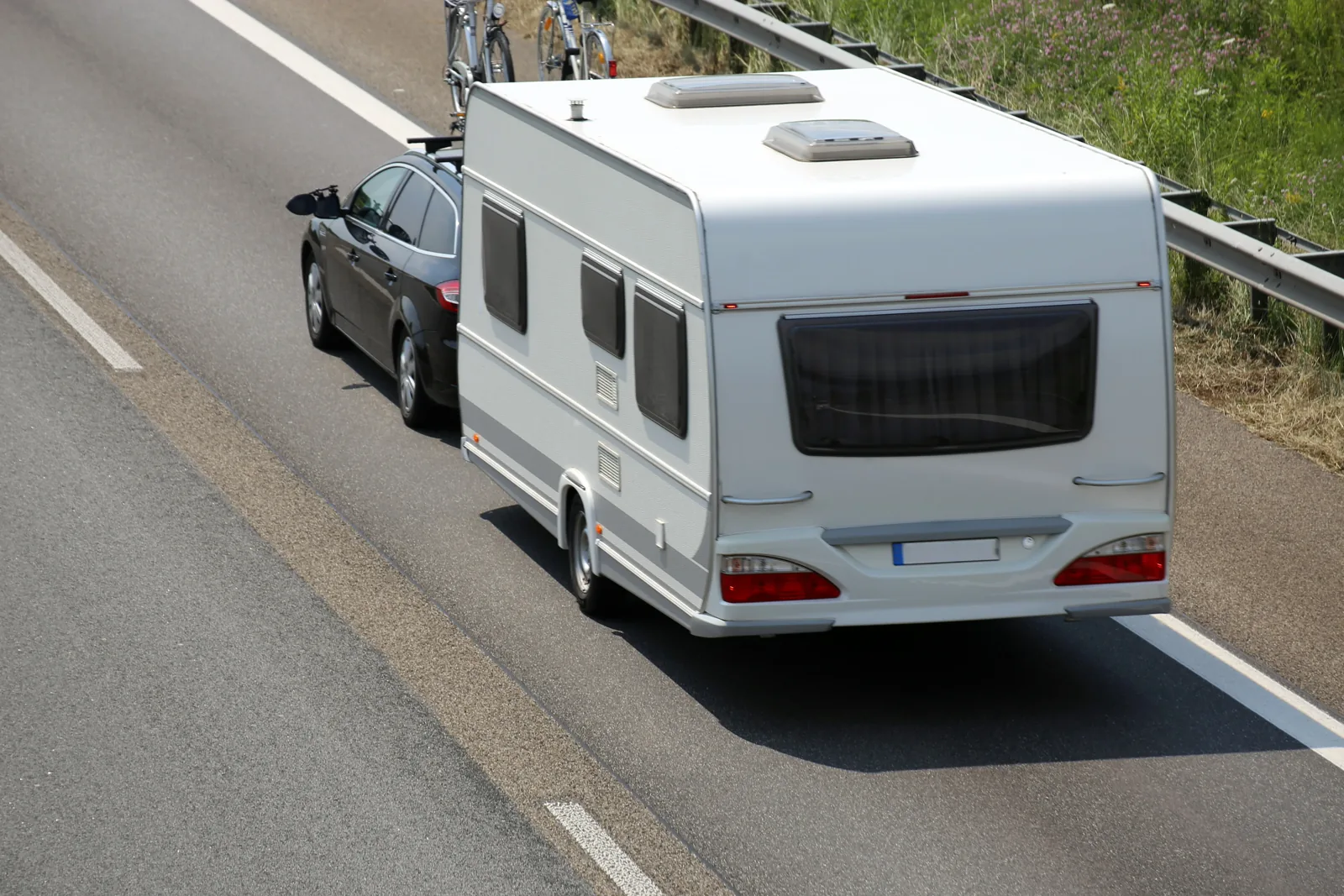 Kombi zieht einen weißen Wohnwagen mit Fahrrädern auf dem Träger über die Autobahn